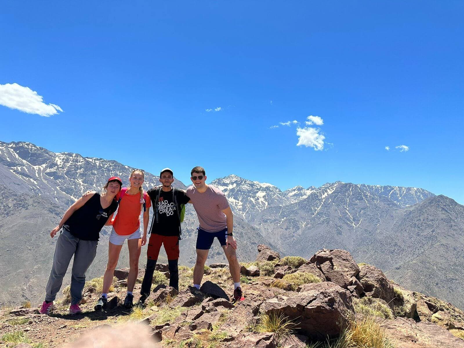 Hikers celebrating at Talamrout Summit with Mount Toubkal in the High Atlas